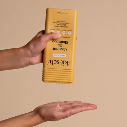 Hand dispensing KITSCH Moisturizing Coconut Oil Shampoo from yellow bottle into palm, beige background