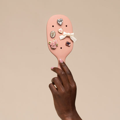 Pink hairbrush with decorative pins held by a hand against a beige background